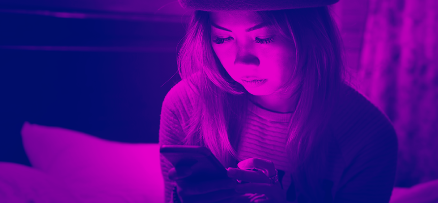 A stylishly dressed young woman sits on a couch staring at her smartphone.